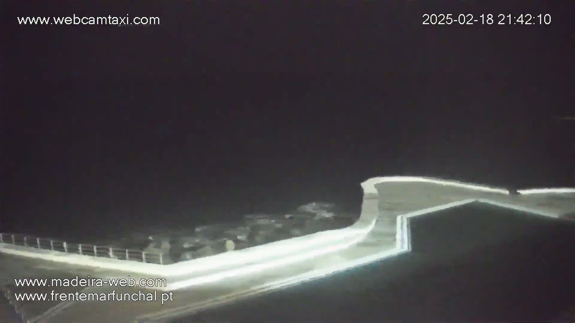 A nighttime, low-angle view shows a section of a light-colored wall or barrier extending into dark water.