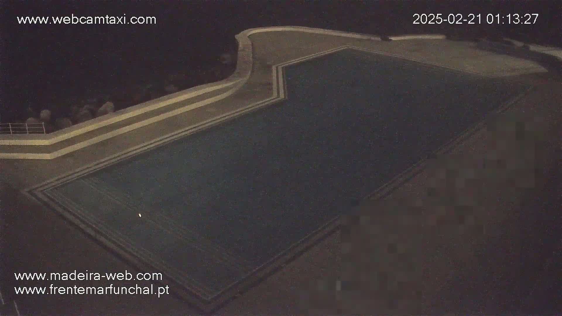 An empty, dark-colored swimming pool is visible at night.