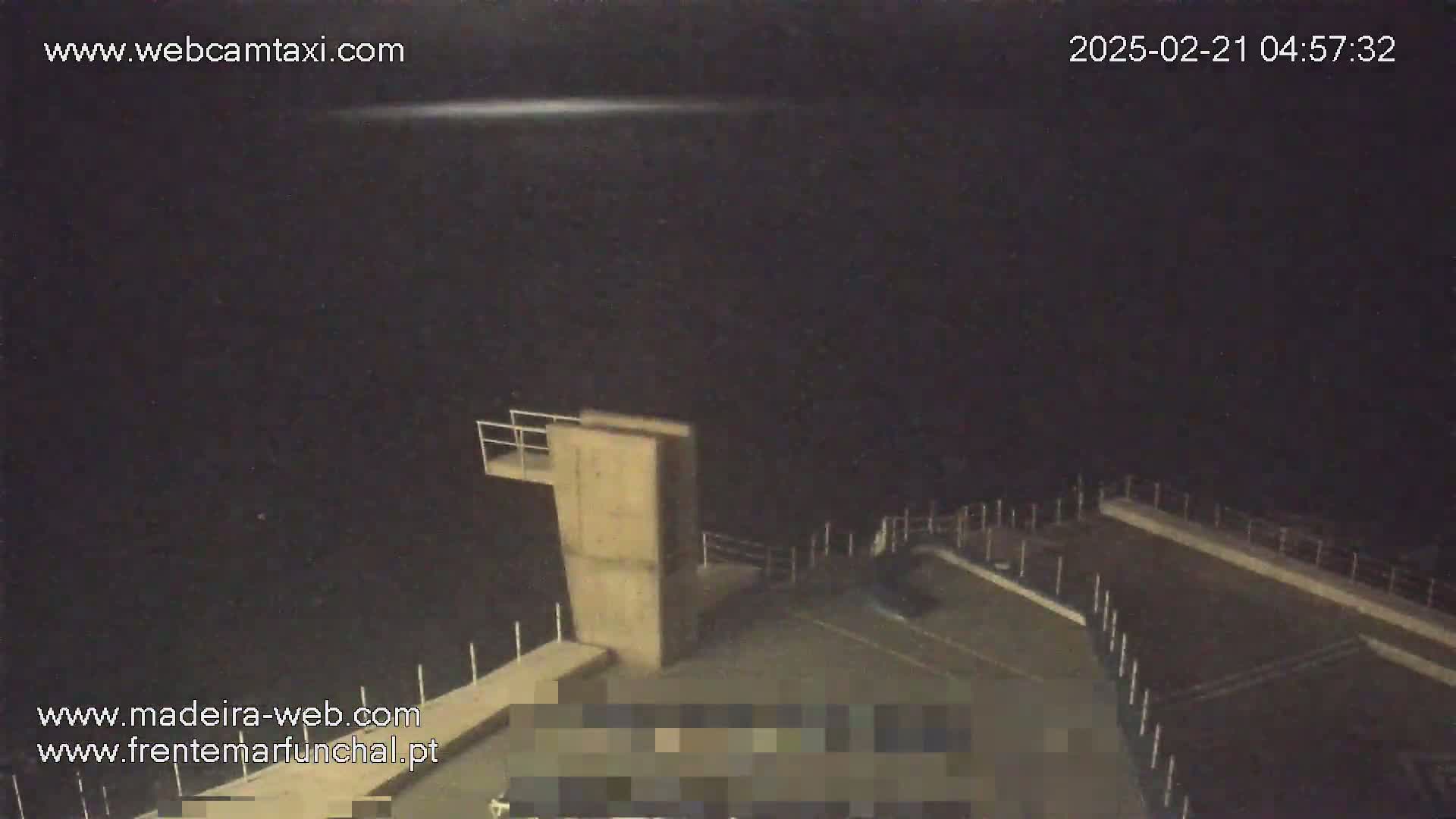 A nighttime, high-angle view shows an empty concrete platform with a small structure and railings, under a dark sky.