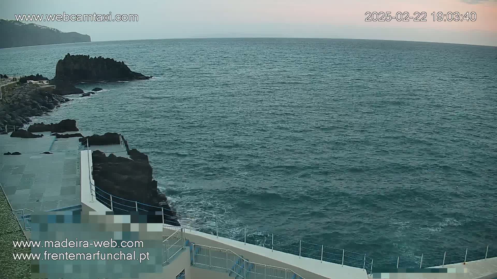 A rocky coastline meets a dark-teal ocean under an overcast sky.