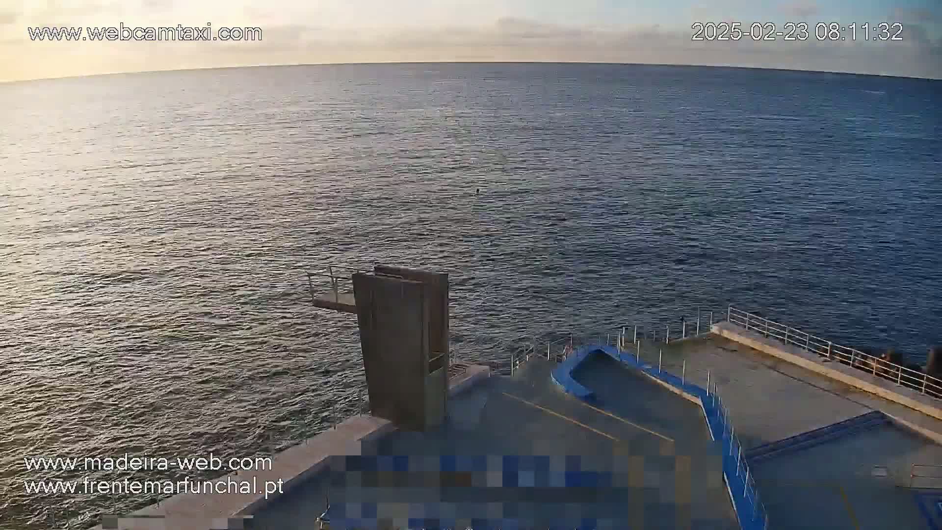 A calm ocean under a partly cloudy sky is viewed from above a diving platform on a concrete structure.