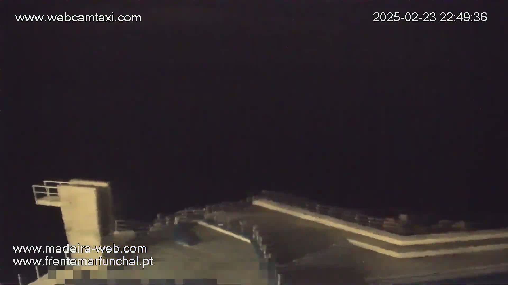 A nighttime view of a low-lit concrete structure, possibly a diving platform or section of a pier, under a dark, overcast sky.