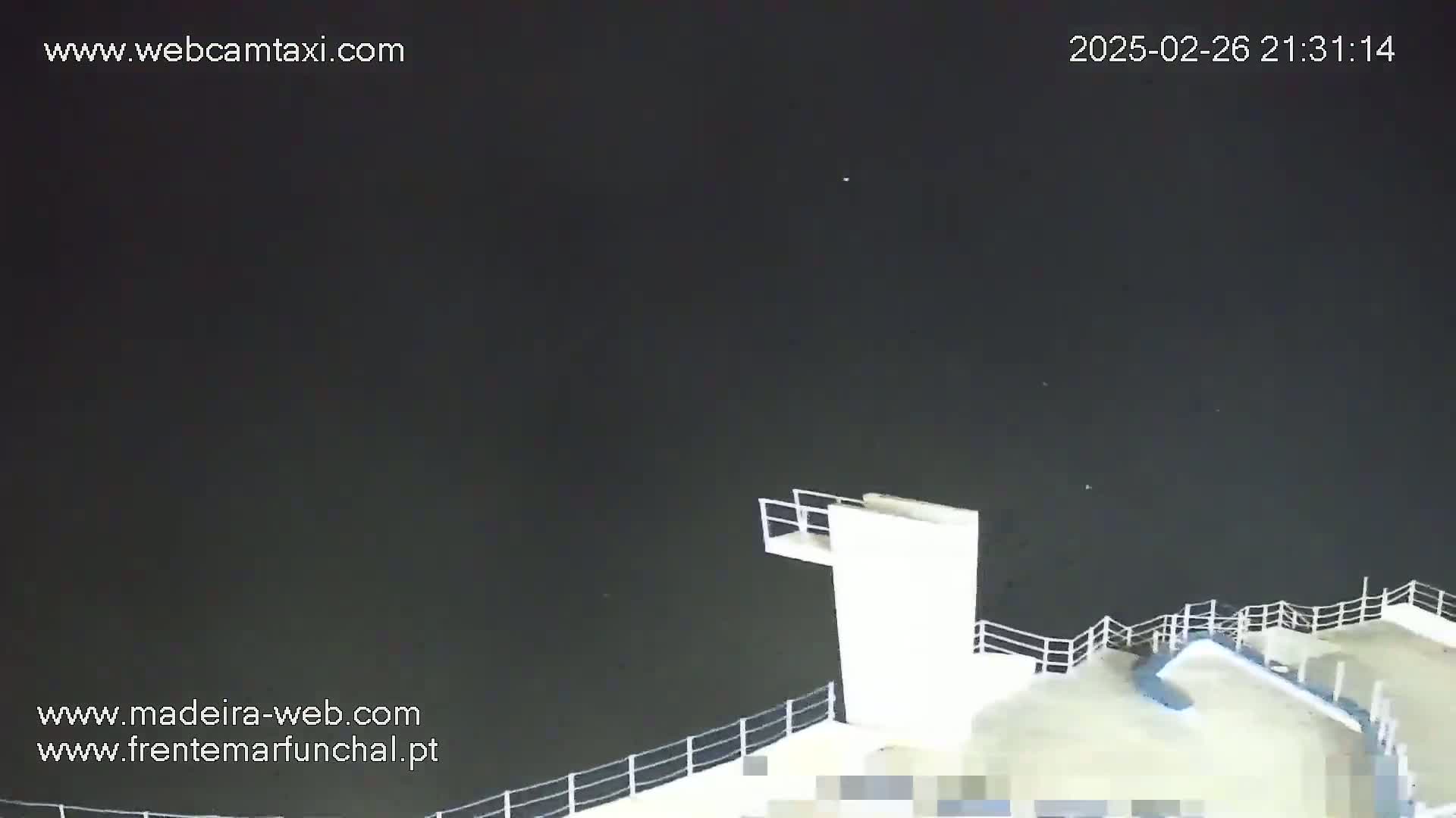 A high-angle nighttime view shows a white diving platform and railing overlooking dark water under a clear, dark sky.