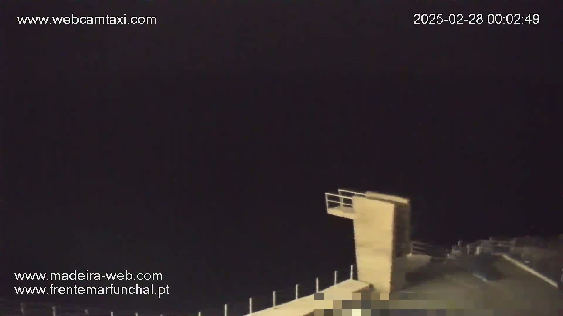 A nighttime, dark image shows a diving platform overlooking a body of water.