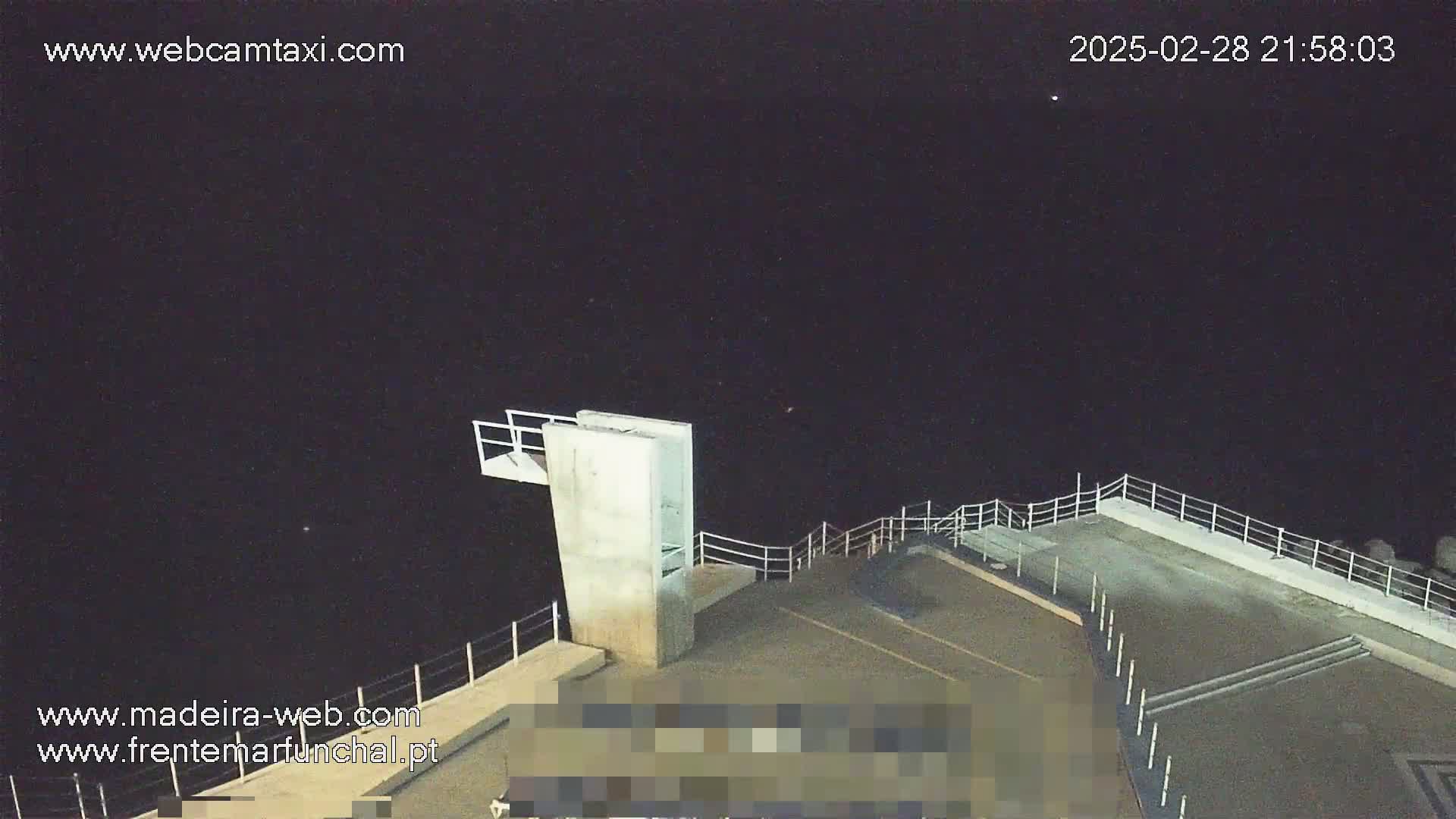 A nighttime, high-angle view shows a concrete diving platform with railings overlooking a dark body of water under a clear, starlit sky.