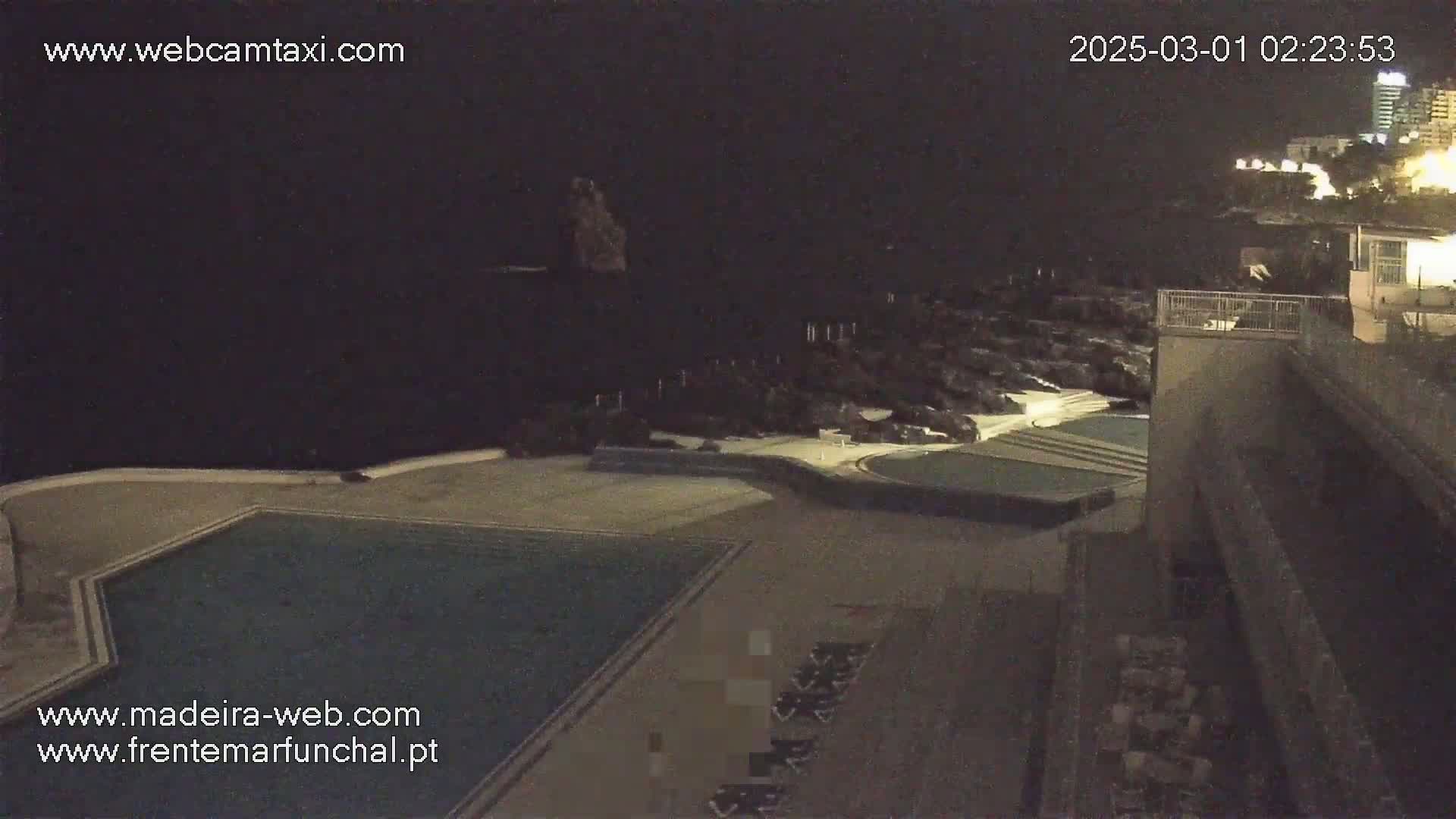 A nighttime view of an outdoor swimming pool and surrounding area, near a dark ocean.