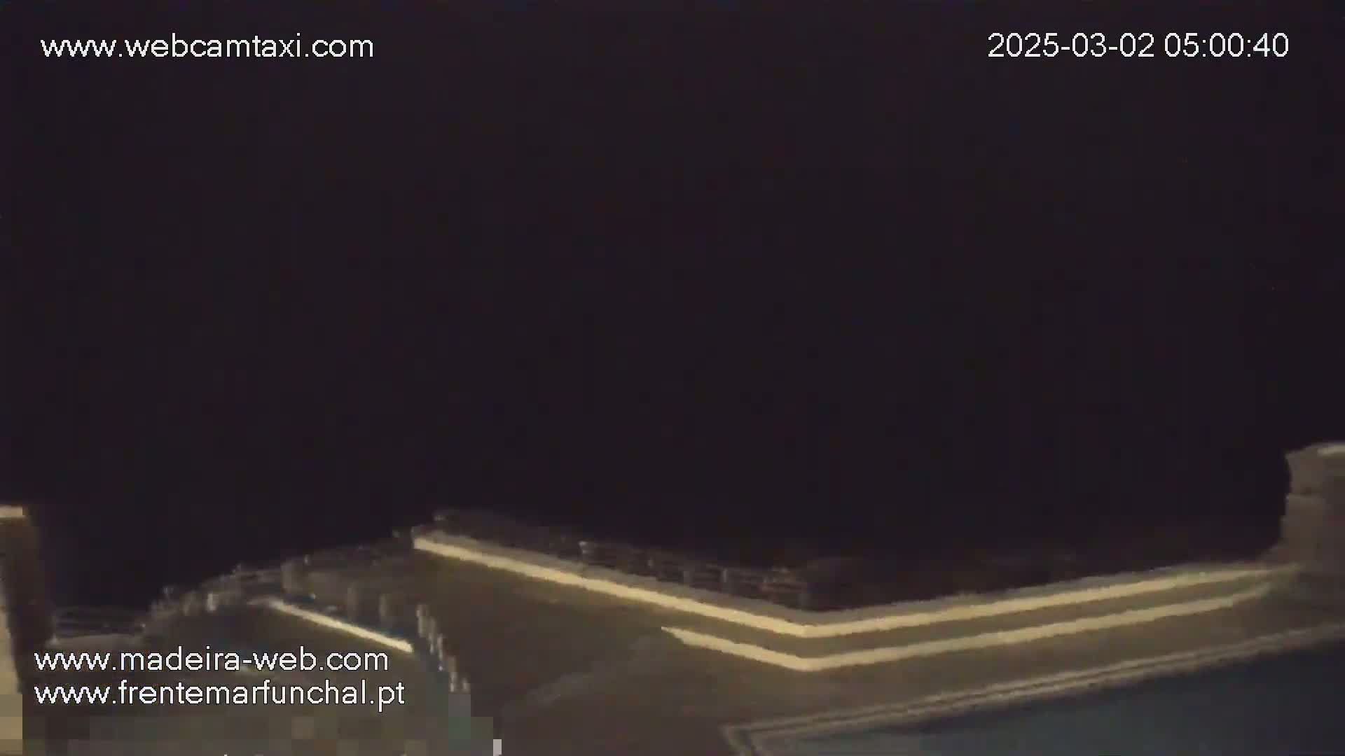 A dark, nighttime view of a low wall or railing, possibly overlooking water, under a completely overcast sky.