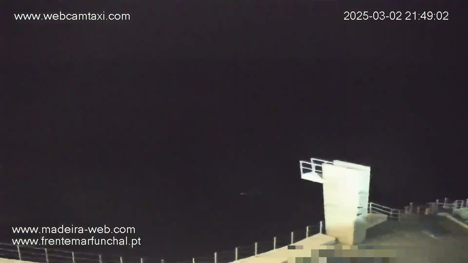 A nighttime, dark view shows a diving platform extending over a very dark body of water.