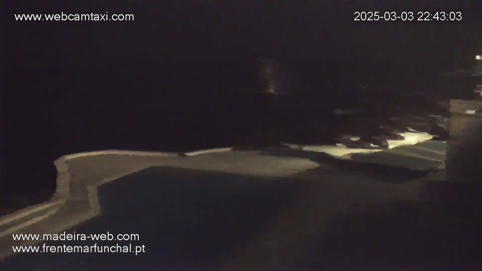 A dark, nighttime scene shows a dimly lit, curved structure, possibly a wall or edge of a building, next to a body of dark water.