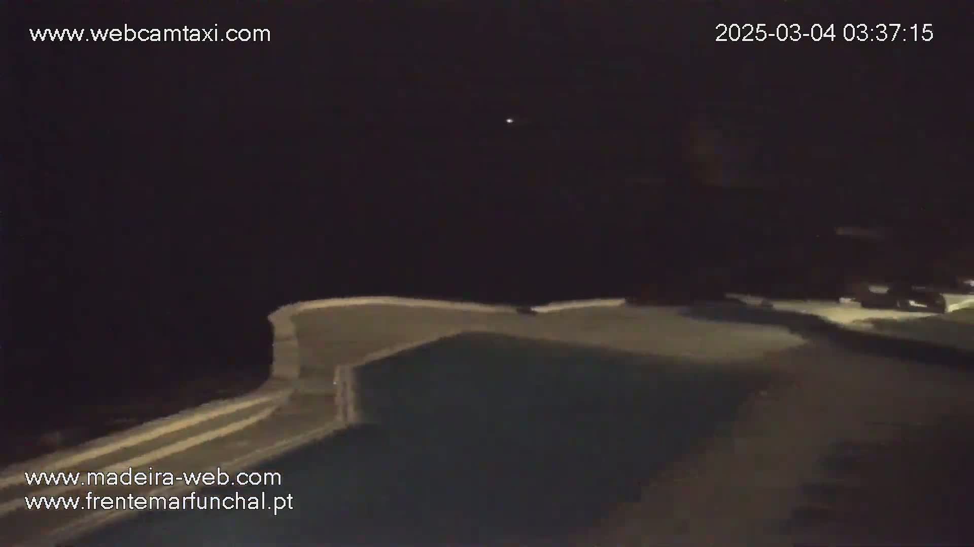 A nighttime view of an empty swimming pool, partially illuminated, with a clear sky and a single distant light visible.
