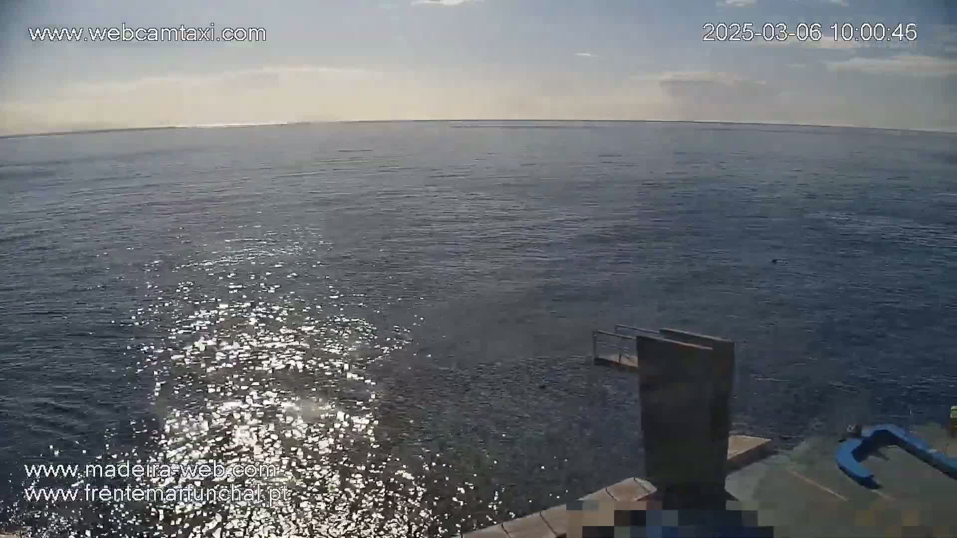 A mostly sunny day shows a calm ocean with a diving platform and sparkling water near the shore.
