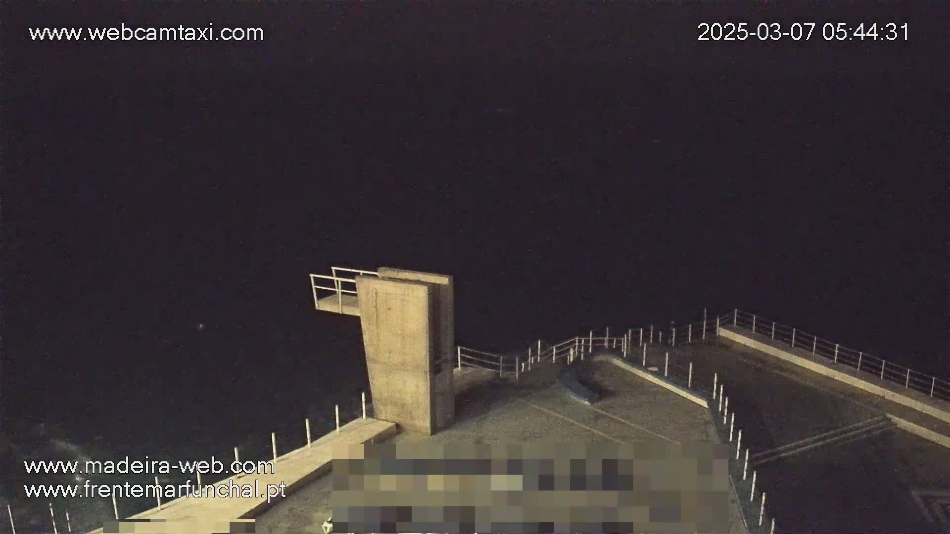A nighttime, high-angle view of a concrete diving platform and surrounding area overlooking a dark body of water under a clear, dark sky.