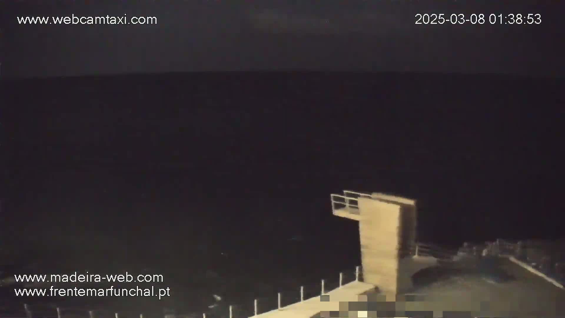 A nighttime, dark view of a body of water shows a diving platform and a railing extending over the water's edge.