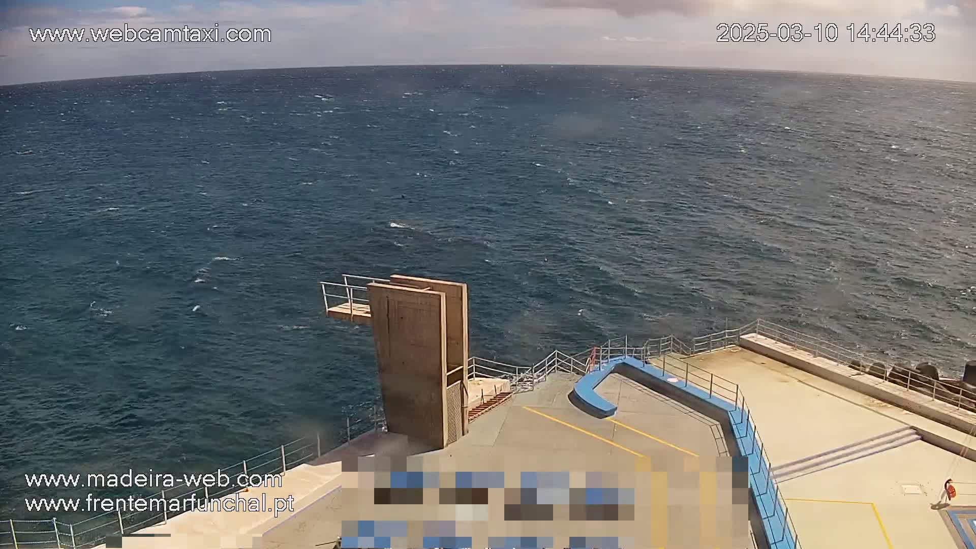 A diving platform overlooks a choppy ocean under a partly cloudy sky.