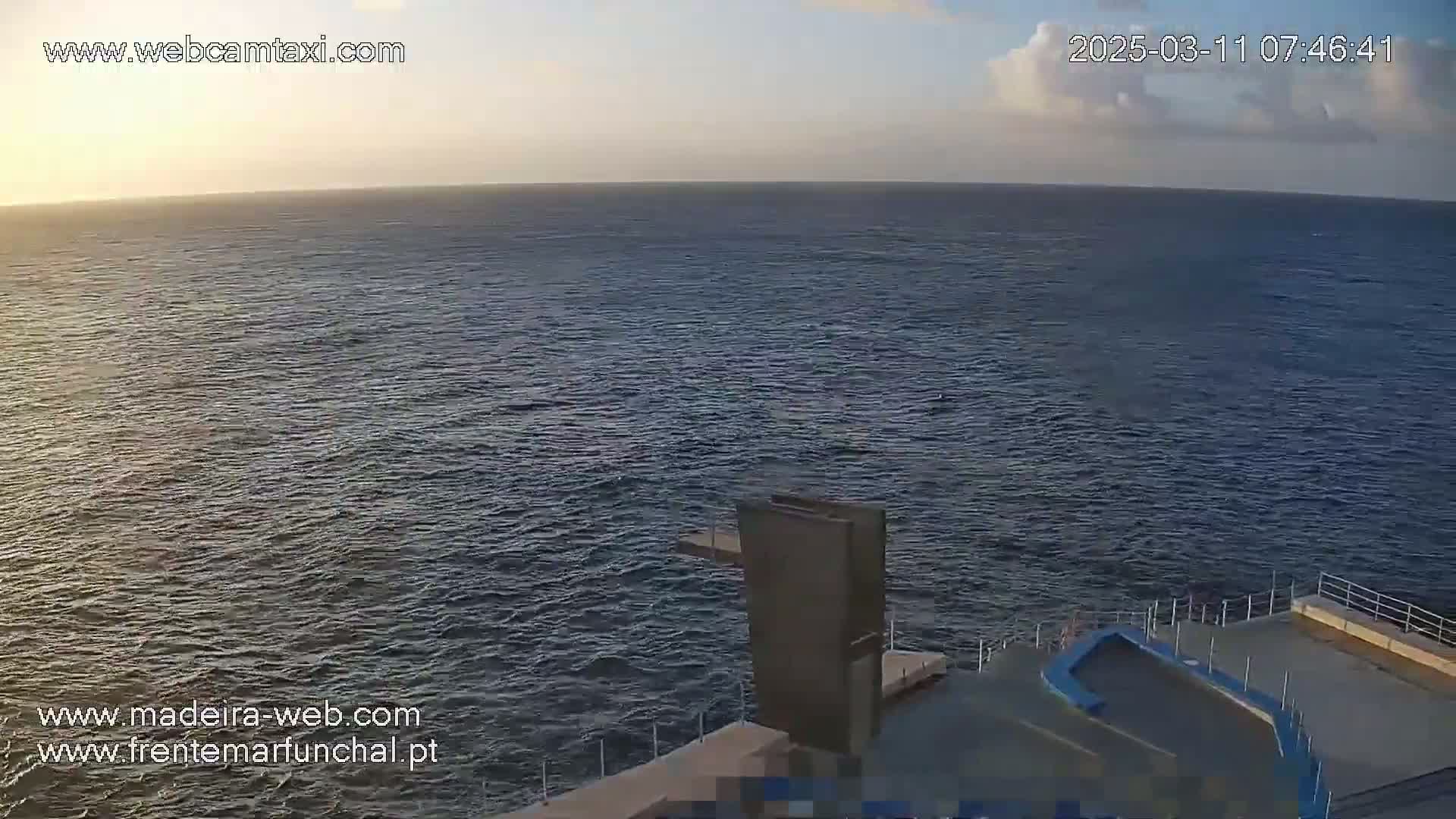 A high-angle, long shot depicts a calm, dark-blue ocean under a mostly clear sky with a few clouds at sunrise, and a diving platform on the right.