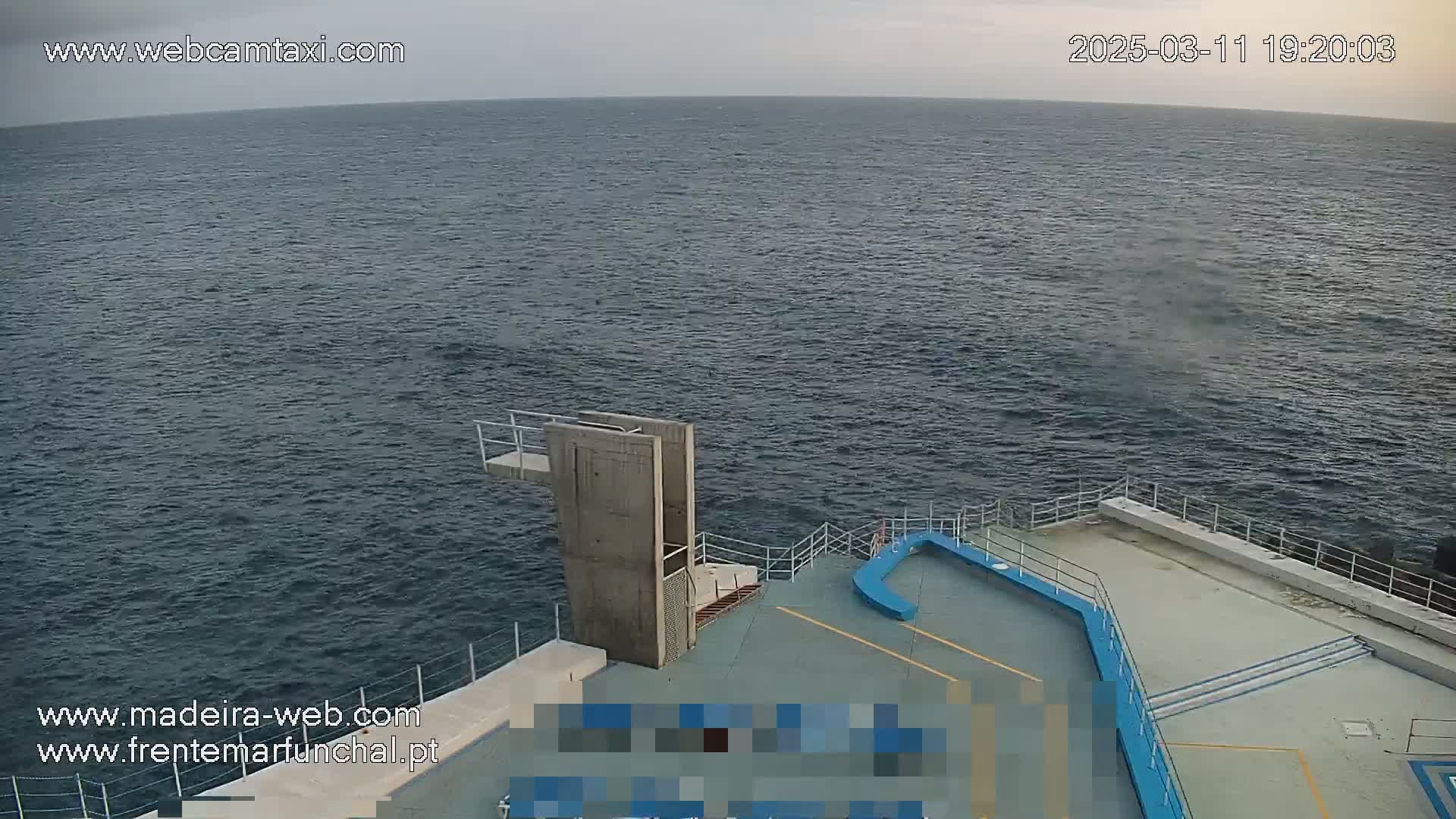 A diving platform extends over a dark-blue, slightly choppy ocean under an overcast sky.
