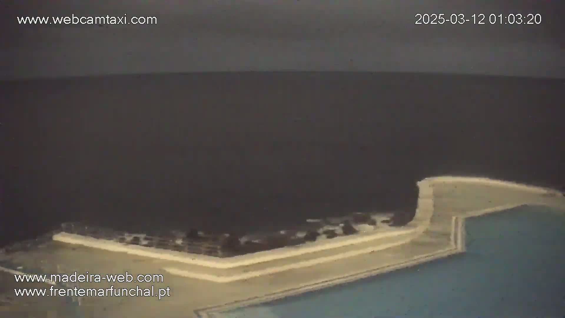 A nighttime view shows a dark ocean meeting a light-colored wall and partially visible swimming pool.