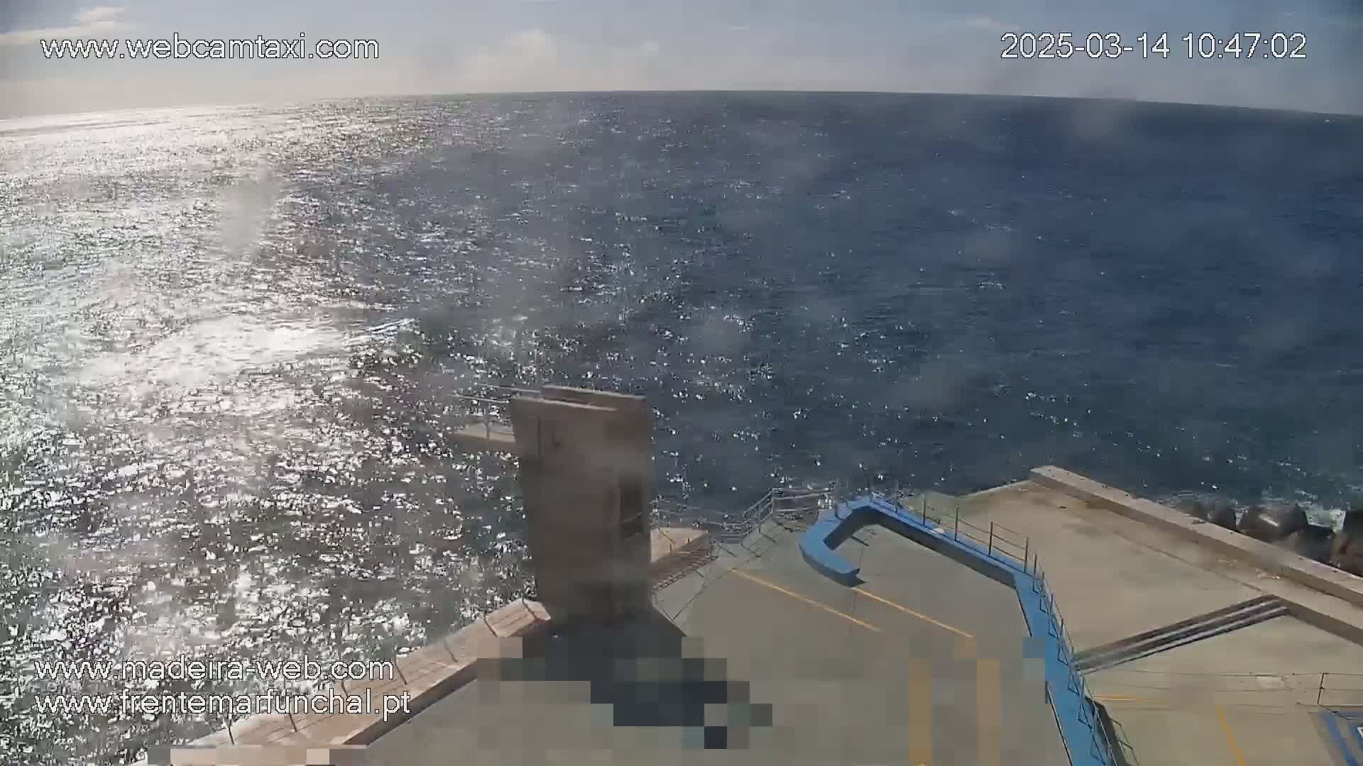 A slightly wavy ocean is viewed from an elevated vantage point overlooking a concrete platform with diving apparatus, under a mostly sunny sky.