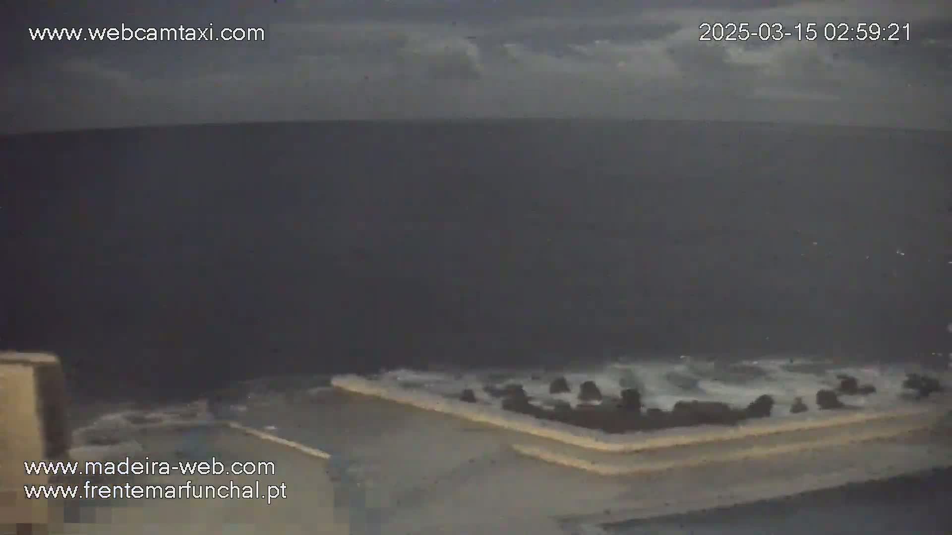 A dark, overcast sky looms over a rough, gray sea crashing against a low, light-colored wall.