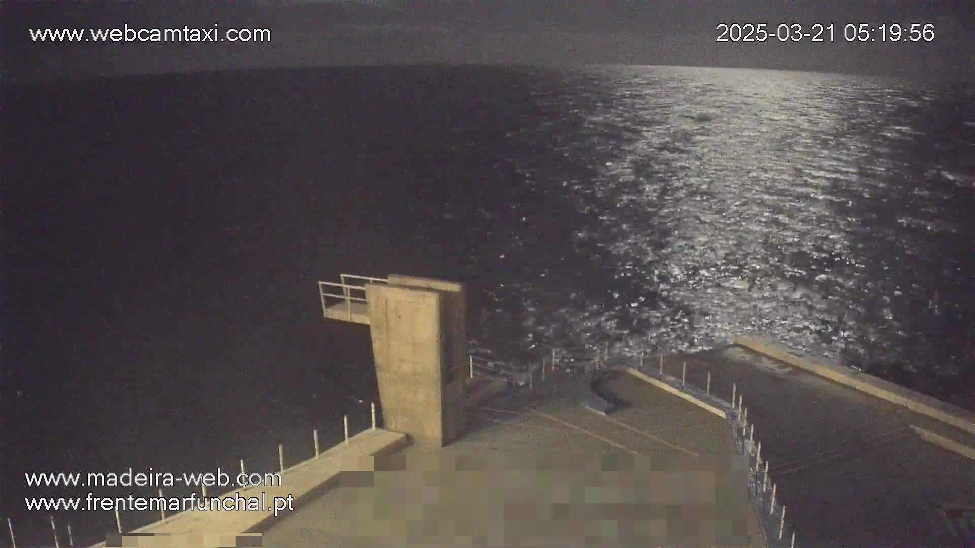 A nighttime view from a high vantage point shows a dark, slightly choppy ocean under a mostly clear sky, with a portion of a structure's deck visible in the foreground.