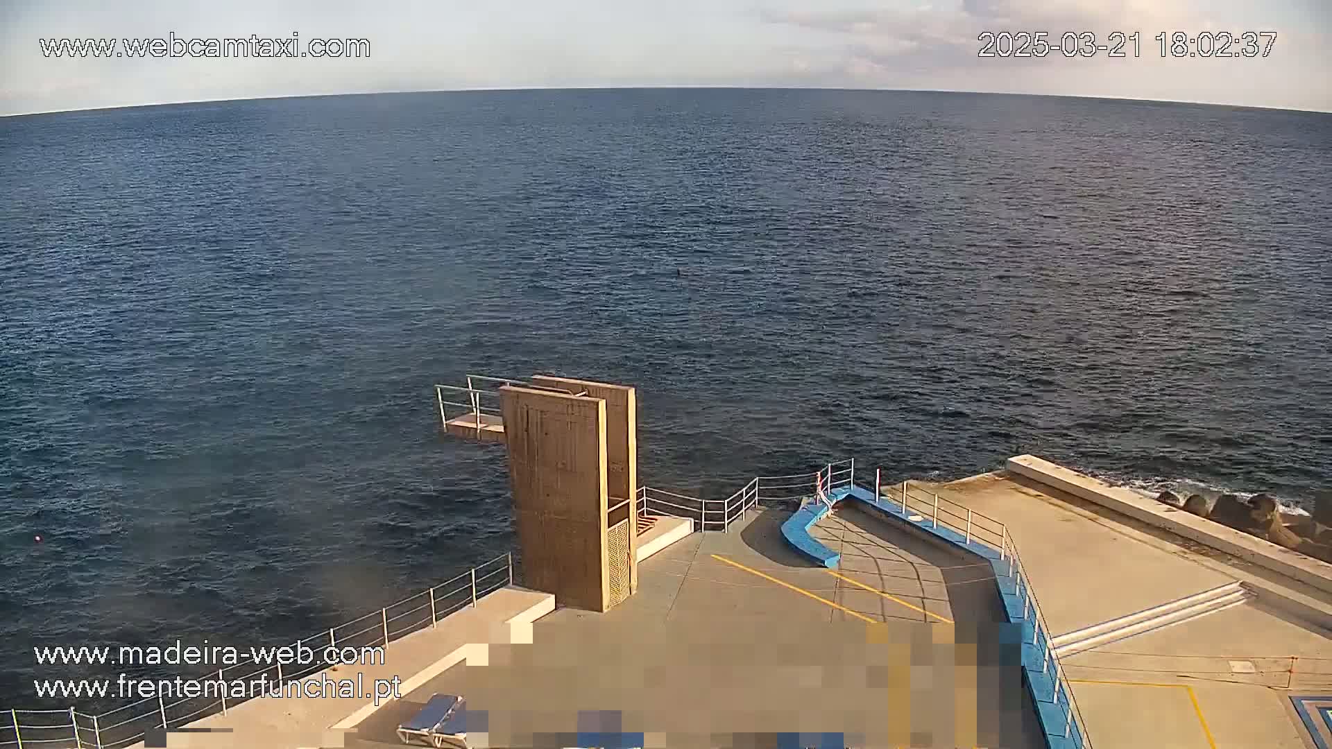 A diving platform stands at the edge of a calm ocean under a mostly clear sky.