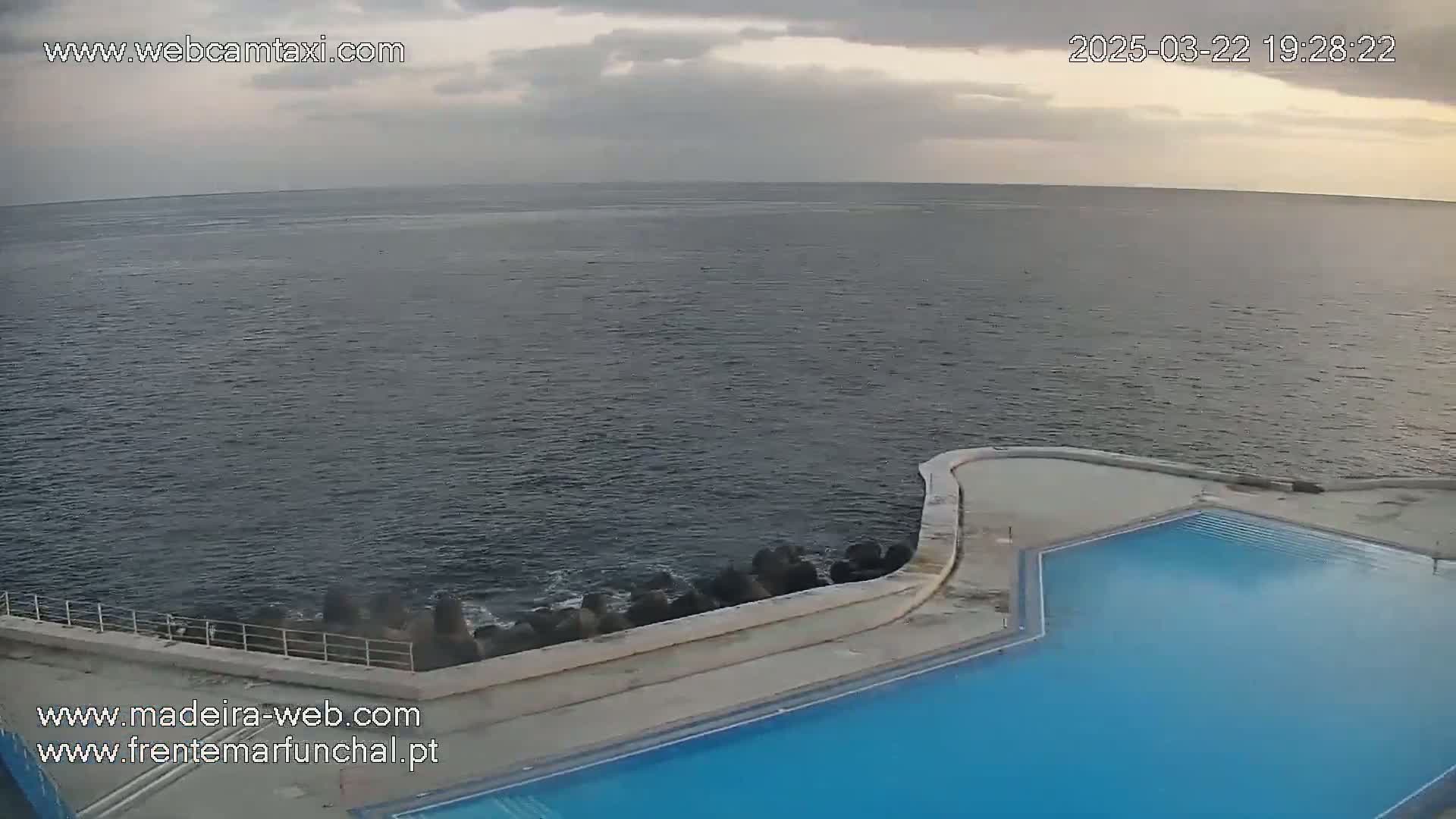 An outdoor pool overlooks a dark, calm ocean under a cloudy sky.