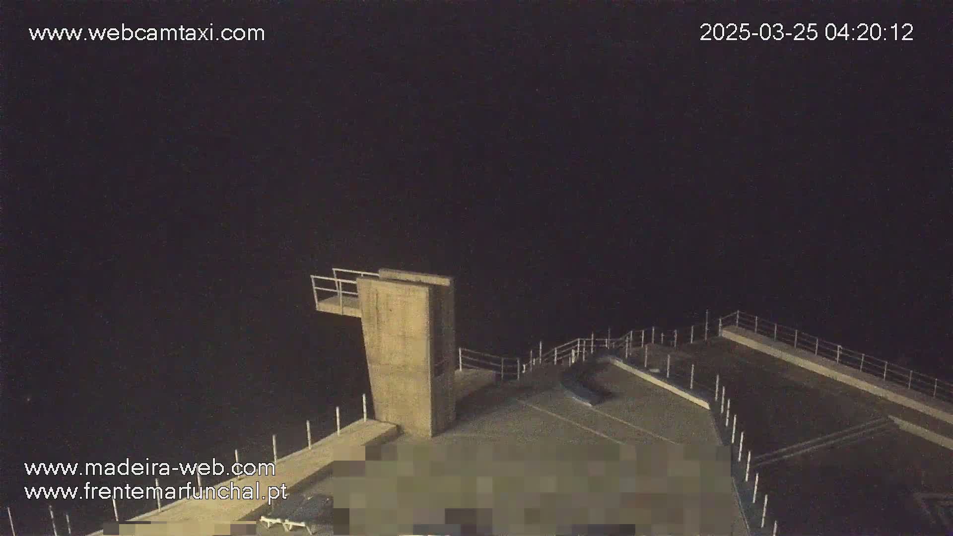 A nighttime view of a concrete diving platform and surrounding area, overlooking a dark body of water under a clear, dark sky.