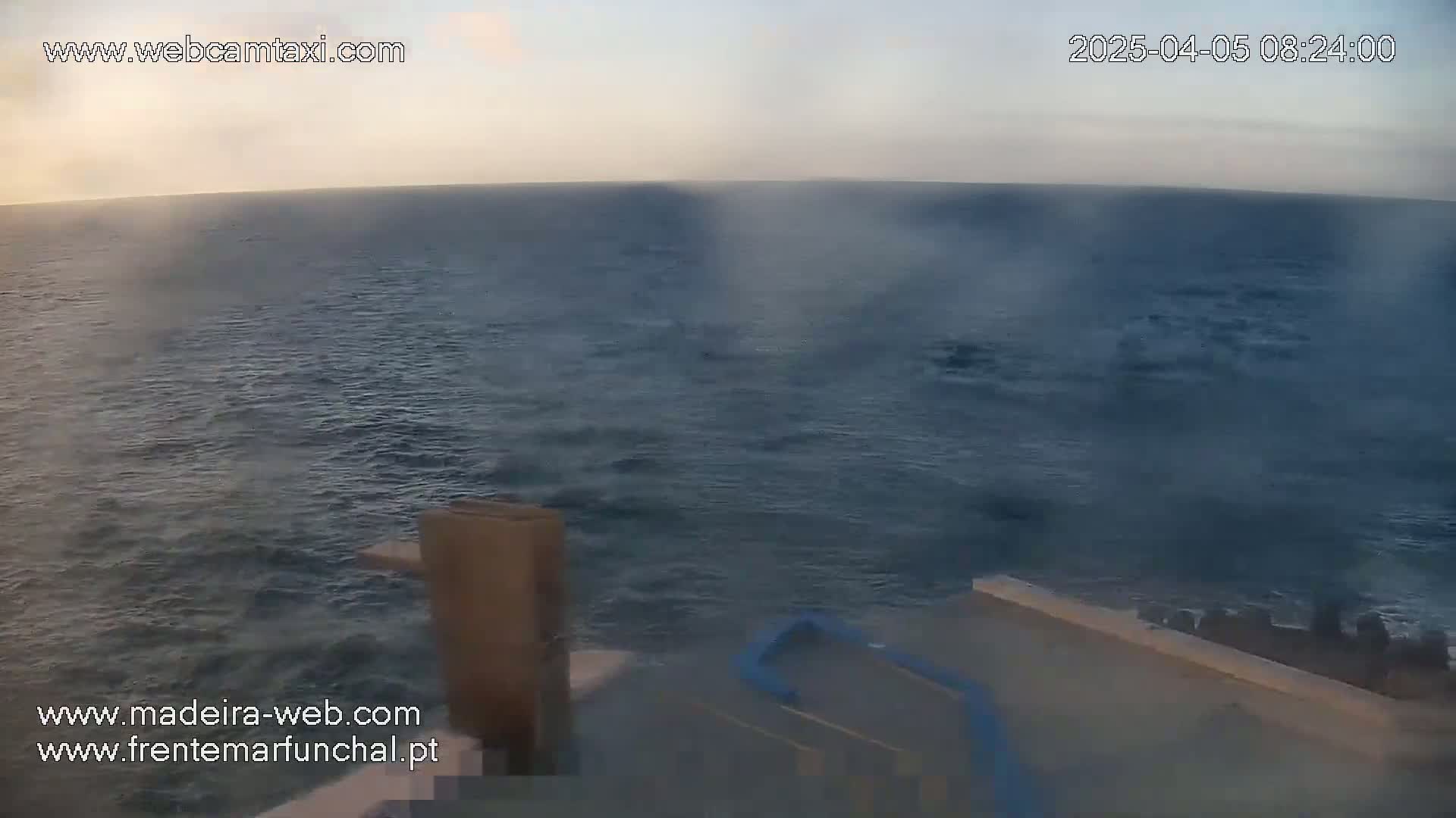A hazy, calm ocean is seen from what appears to be a ship's deck at dawn or dusk.