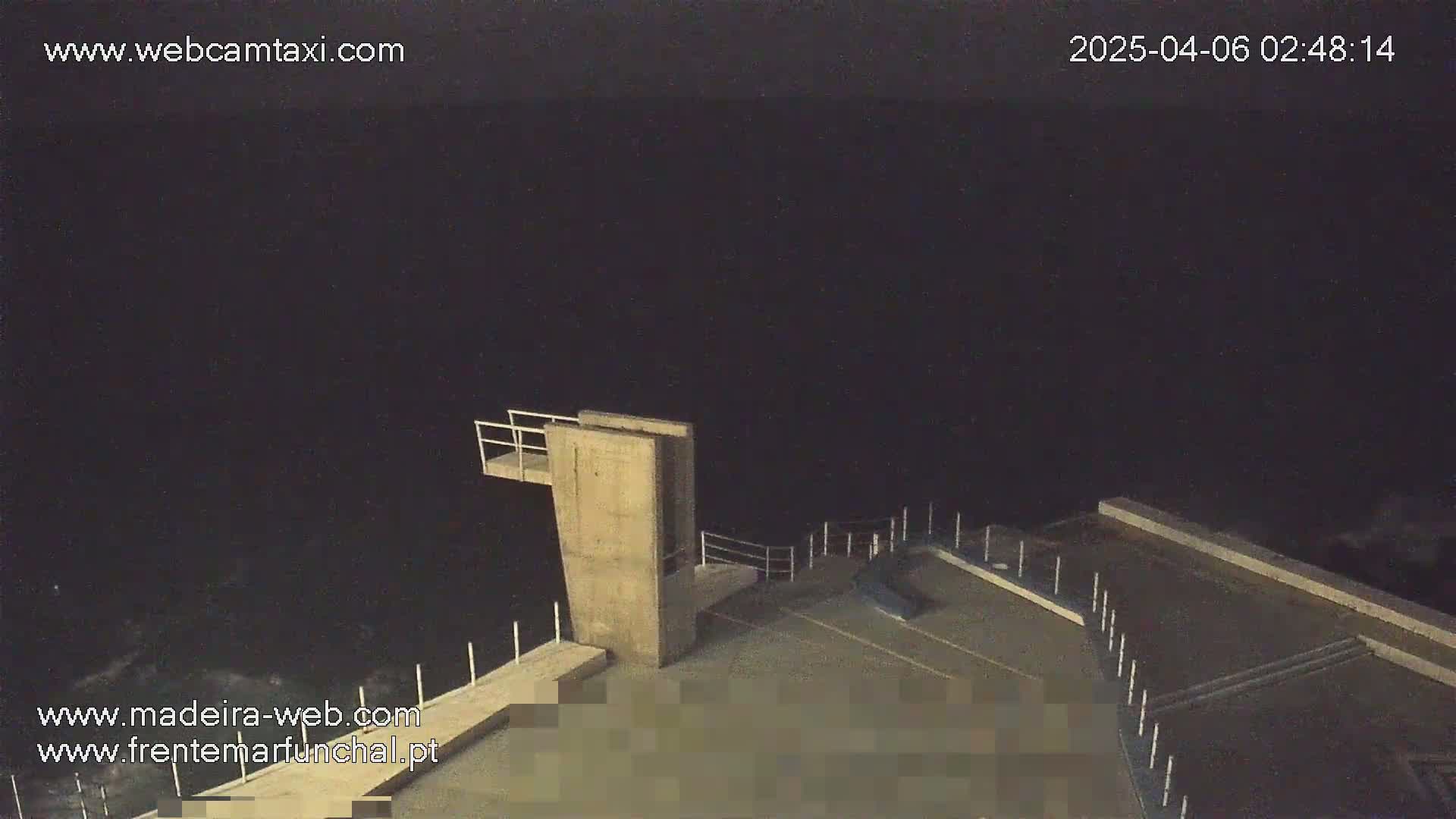 A high-angle nighttime view shows a concrete diving platform overlooking a dark body of water under a clear, dark sky.