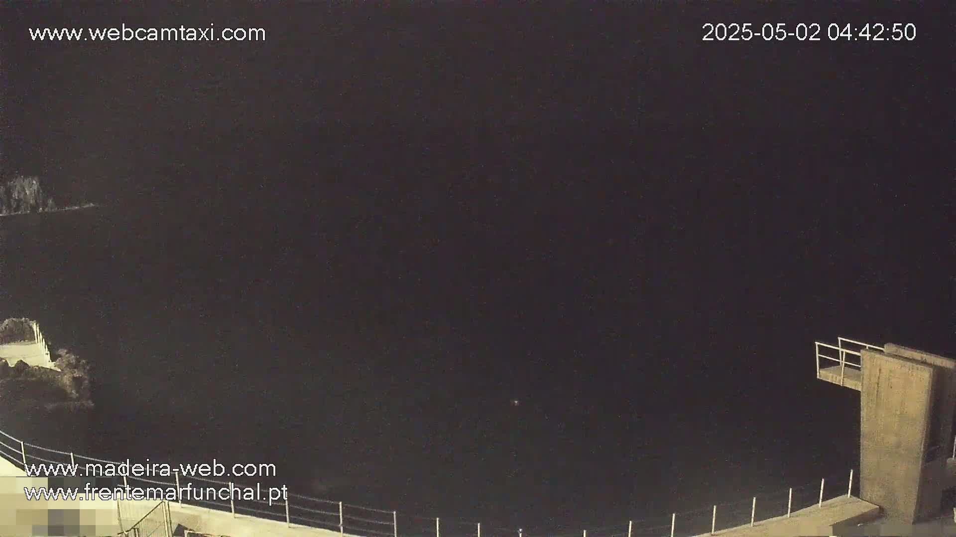 A nighttime view of dark water below a low concrete structure with a diving platform.