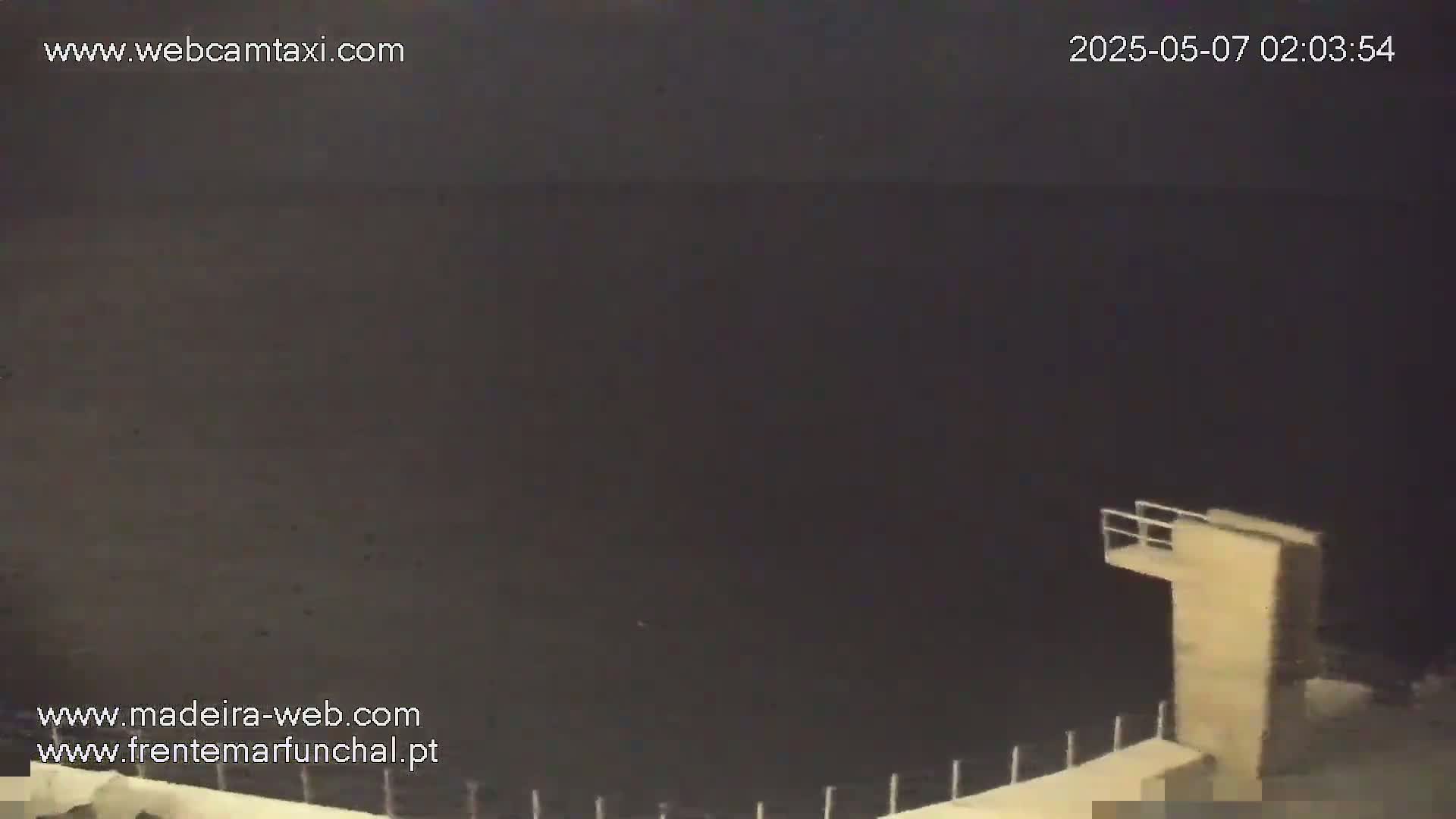 A dark, nighttime view of a body of water with a small diving platform visible in the lower right corner.
