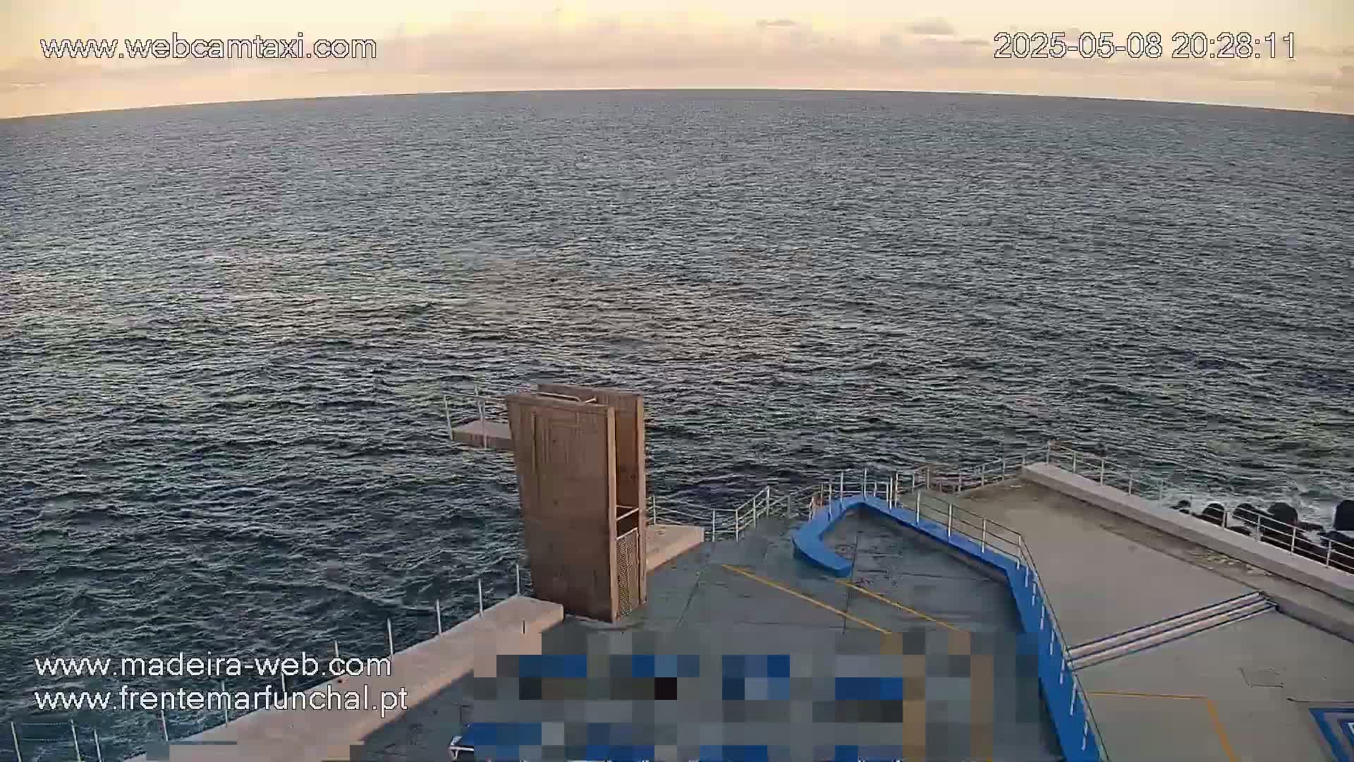 A high-angle, twilight view shows a concrete platform extending into a dark-blue ocean, featuring a wooden diving structure and a curved blue section.