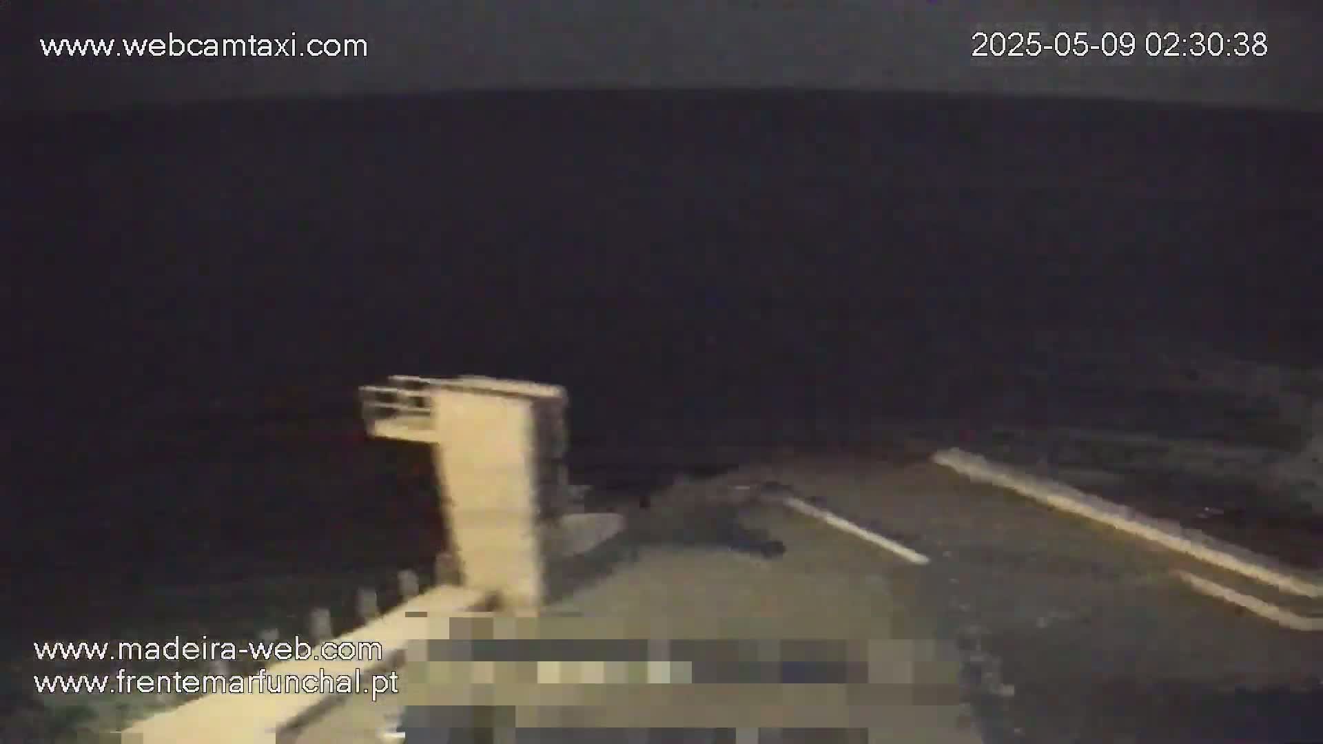 A nighttime, low-light view shows a portion of a light-colored structure next to a dark body of water.