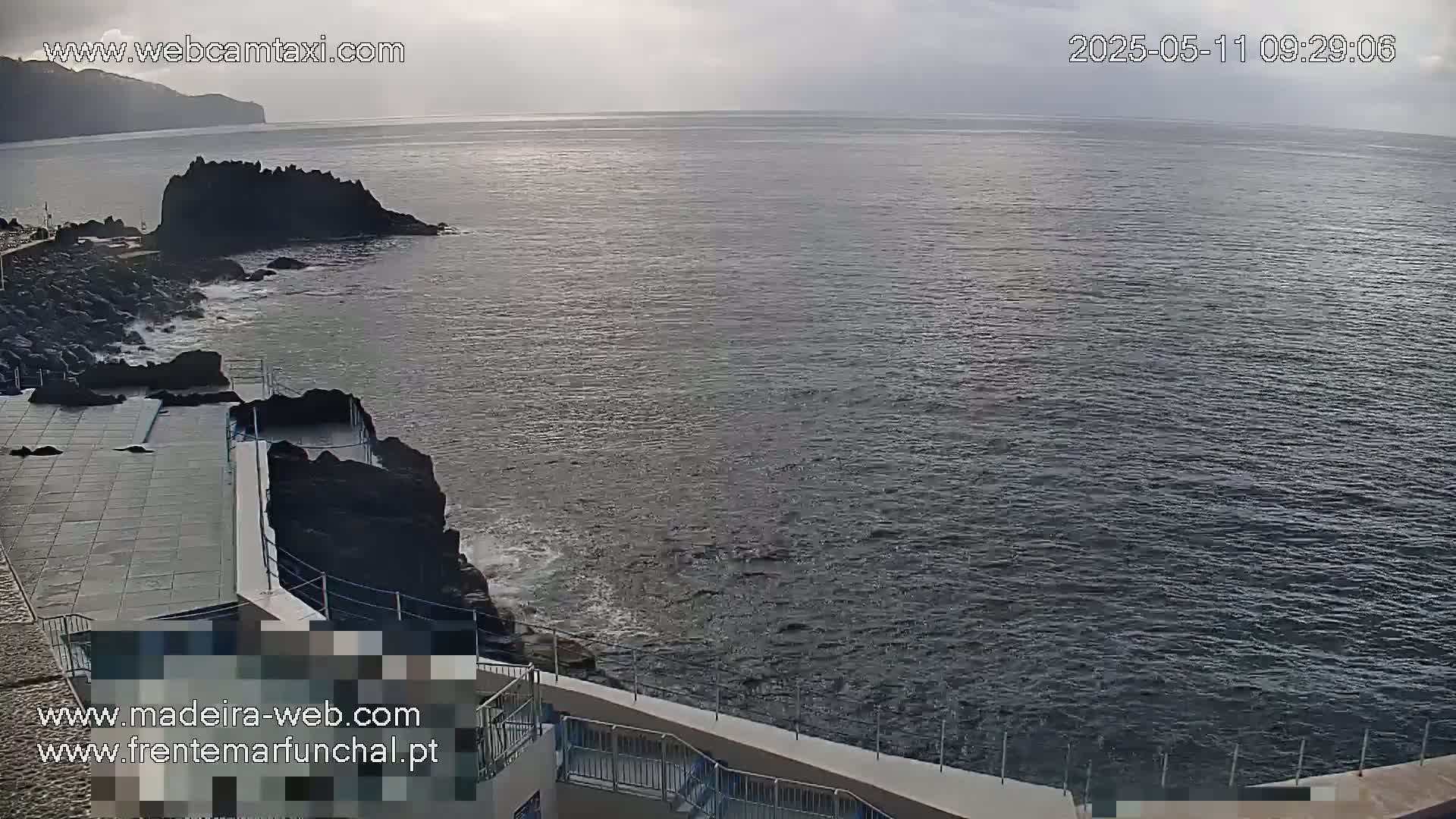 A rocky coast with a concrete platform and railings overlooks a dark, somewhat choppy ocean under an overcast sky.