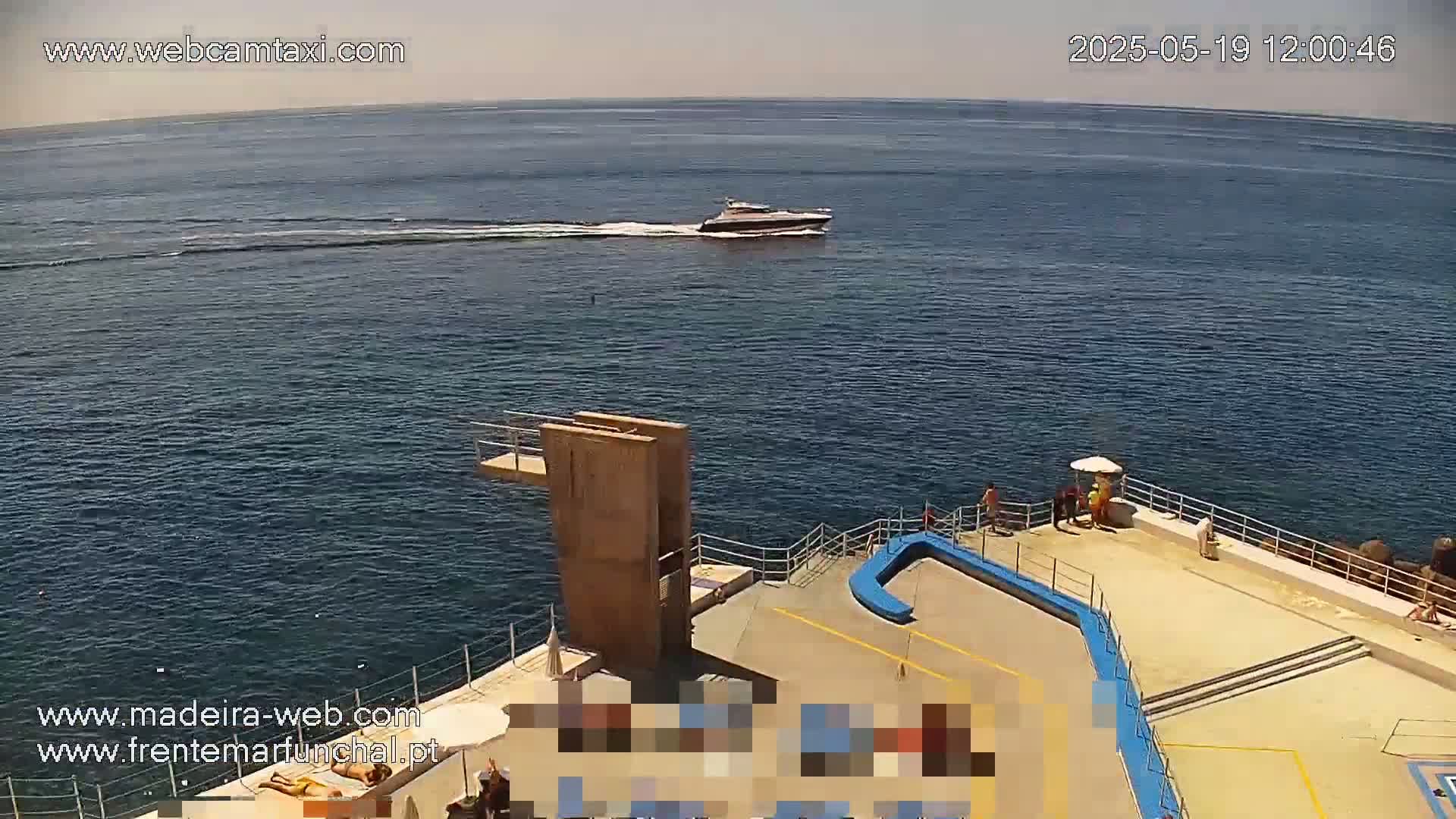 A boat travels across a calm, sunny ocean toward a diving platform and sunbathing area with several people present.