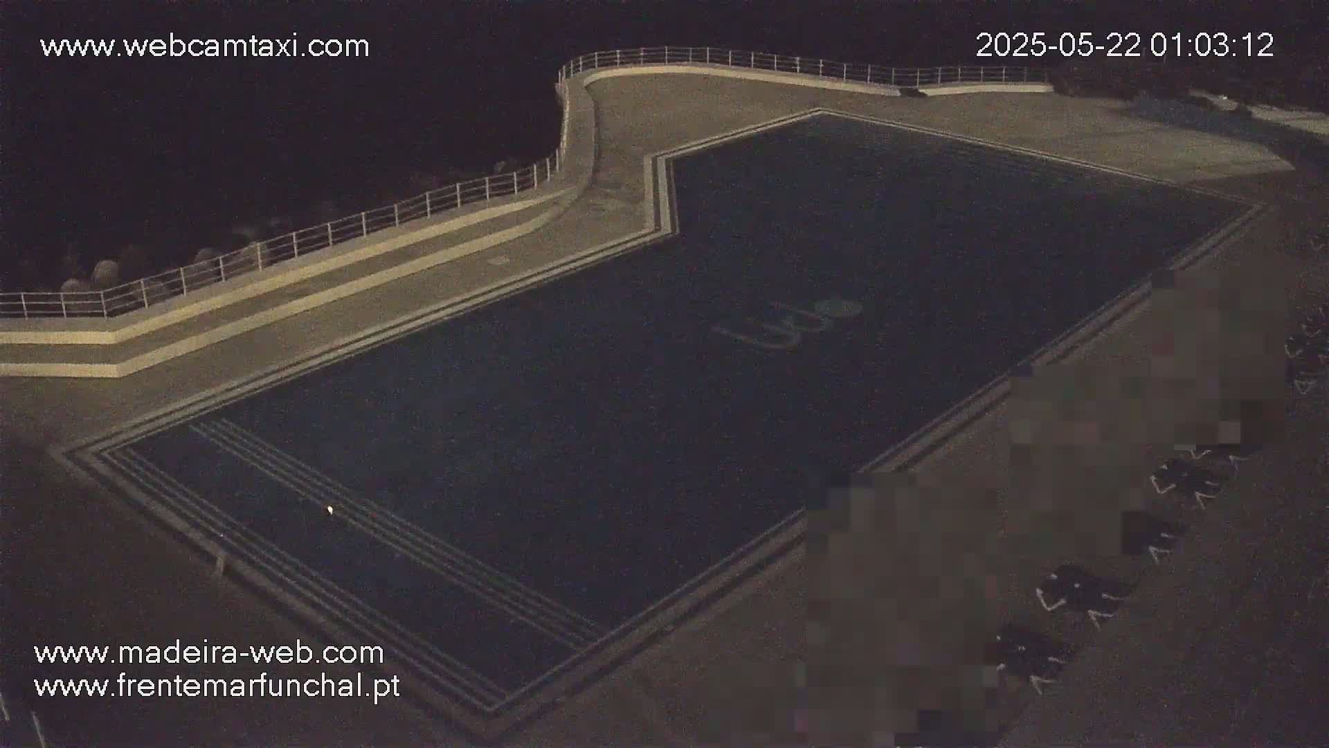 An empty, dark-blue outdoor swimming pool is seen at night.