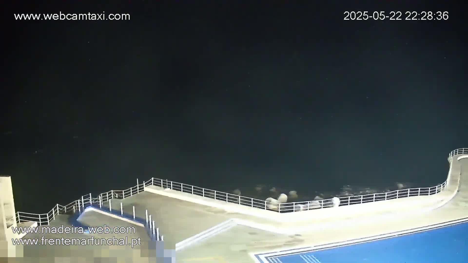 A nighttime view of a concrete seawall with a railing overlooking dark water.