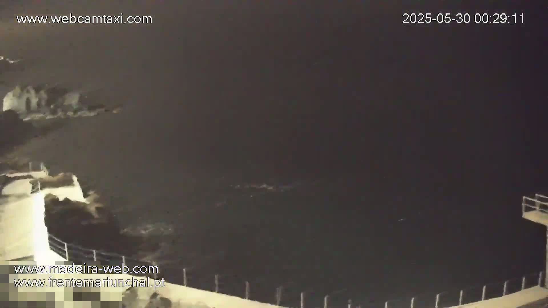 A nighttime view of dark ocean water crashing against a rocky shoreline.