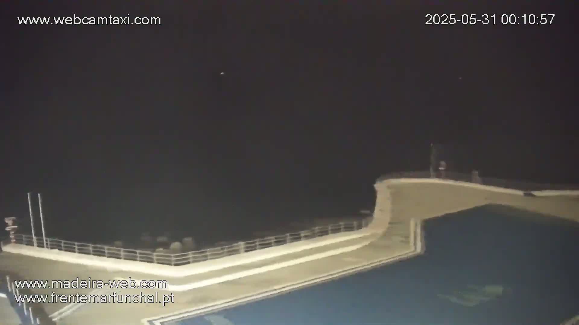 A nighttime view of an outdoor pool area with a wall and railing overlooking a dark ocean under a clear sky.