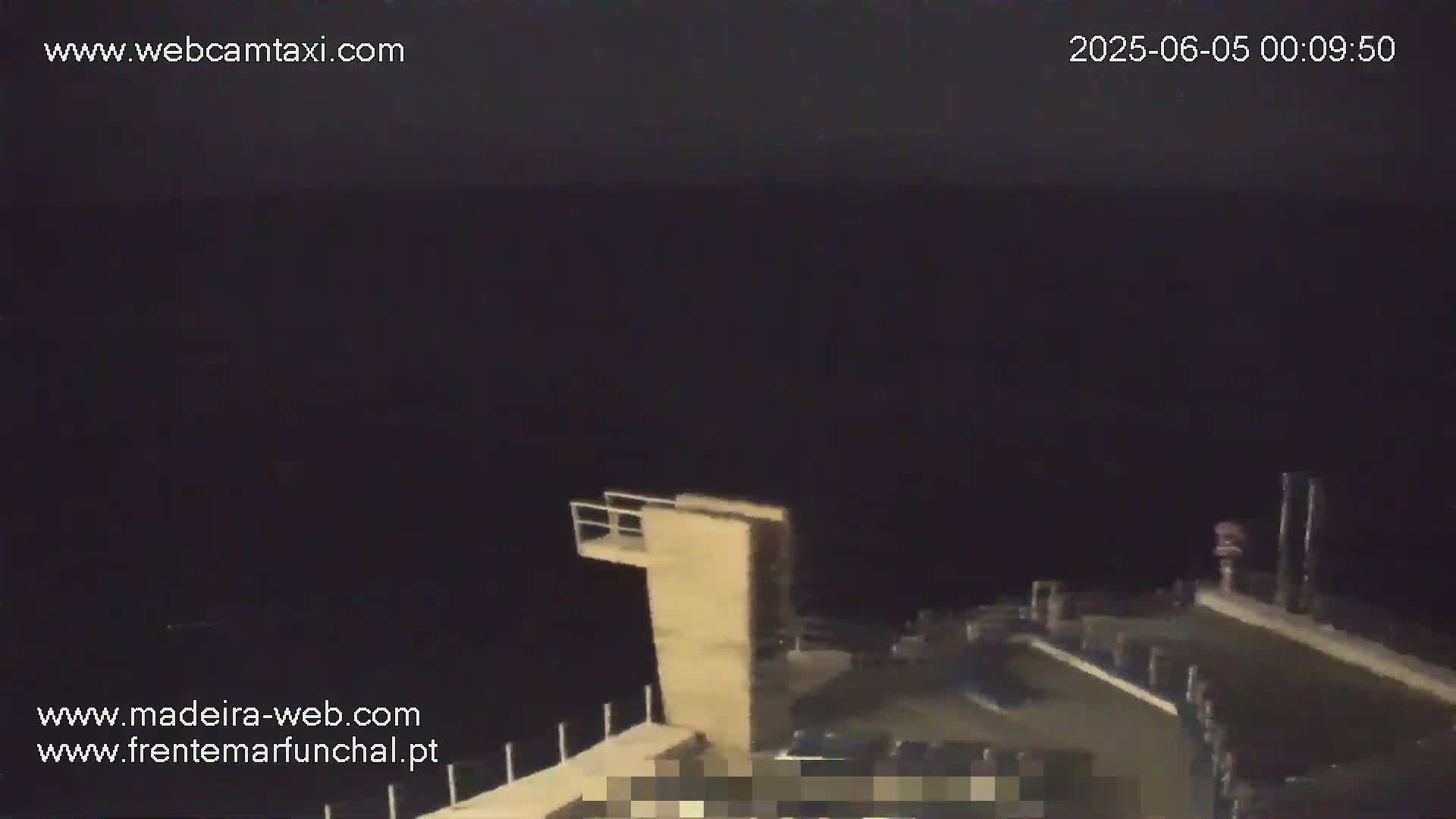 A nighttime view shows a dark body of water, a diving platform, and a partially visible dock under a dark sky.