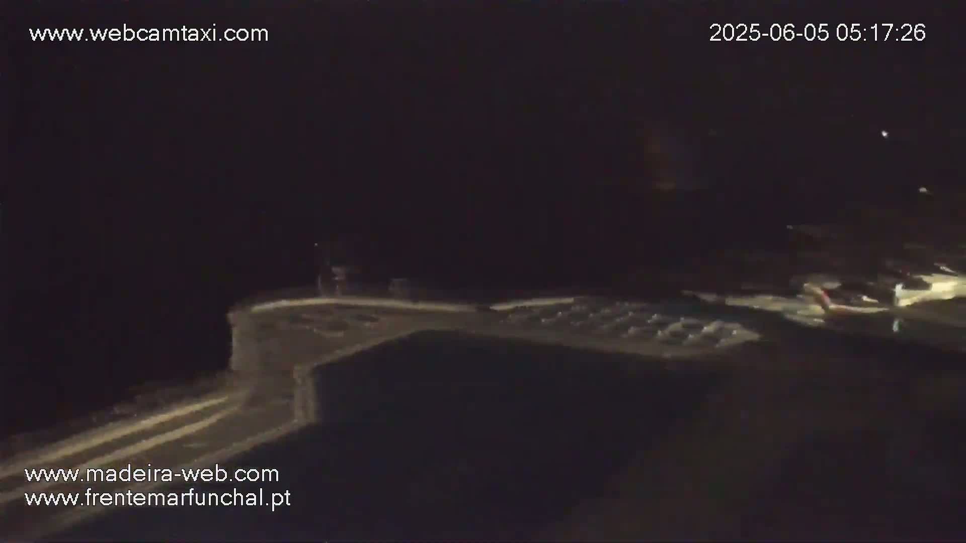 A dark, nighttime scene shows a dimly lit outdoor area with a structure resembling a pool deck or patio.