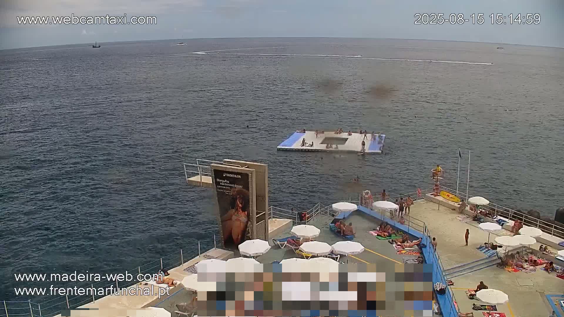 A mostly sunny day shows a rocky coastline with a deck of lounge chairs overlooking a calm ocean with a distant ship.