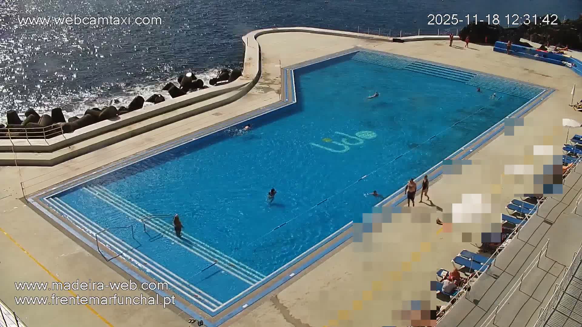 A mostly sunny day shows a rocky coastline with a deck of lounge chairs overlooking a calm ocean with a distant ship.