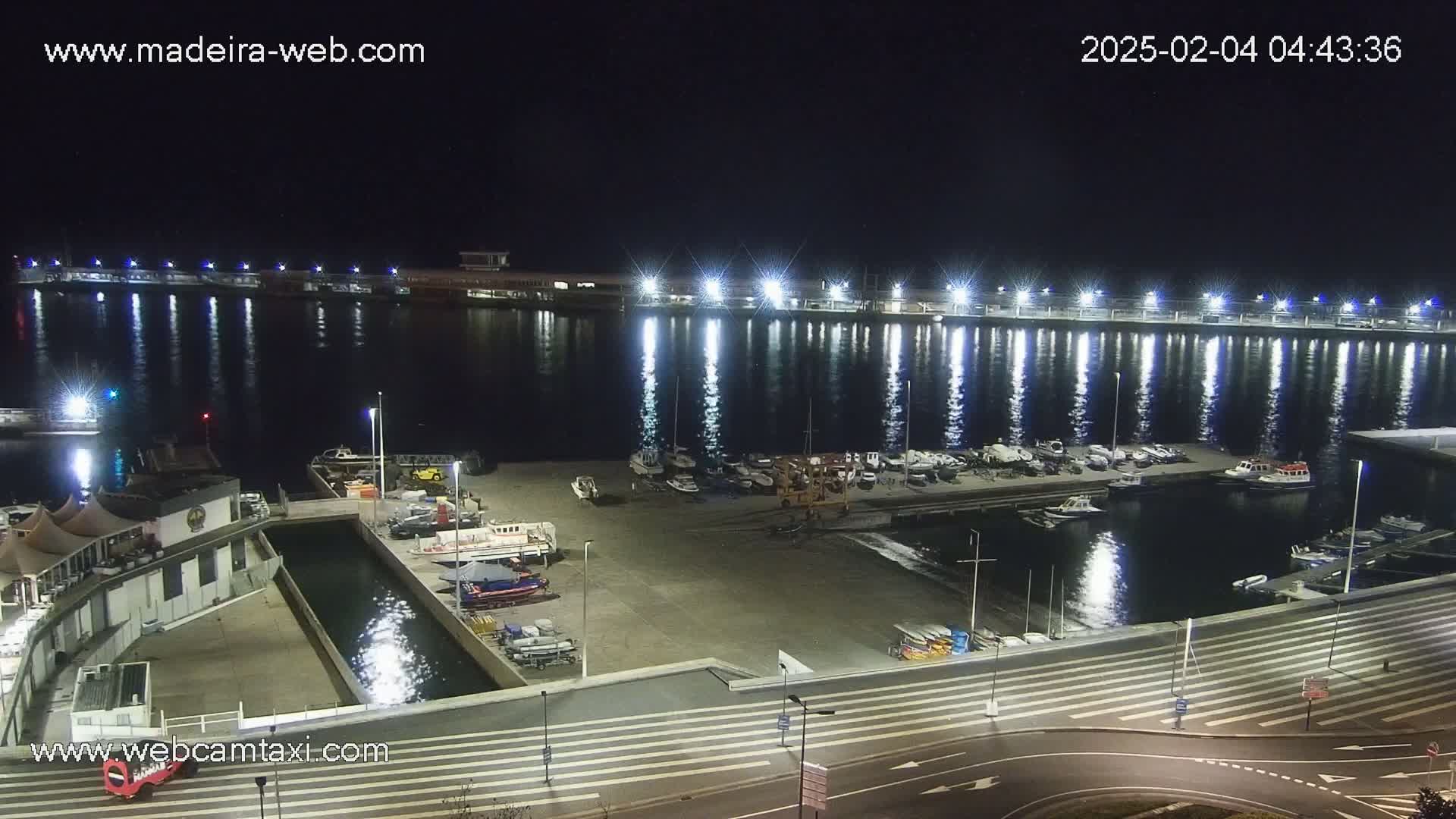 A nighttime view of a marina filled with boats, illuminated by lights reflecting on calm water.