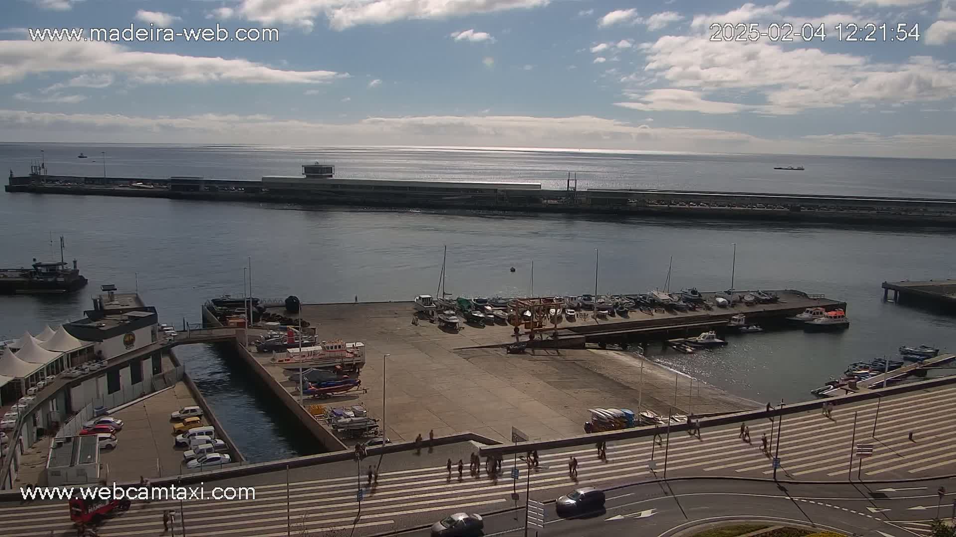 A harbor with docked boats and a pedestrian crossing under partly cloudy skies.