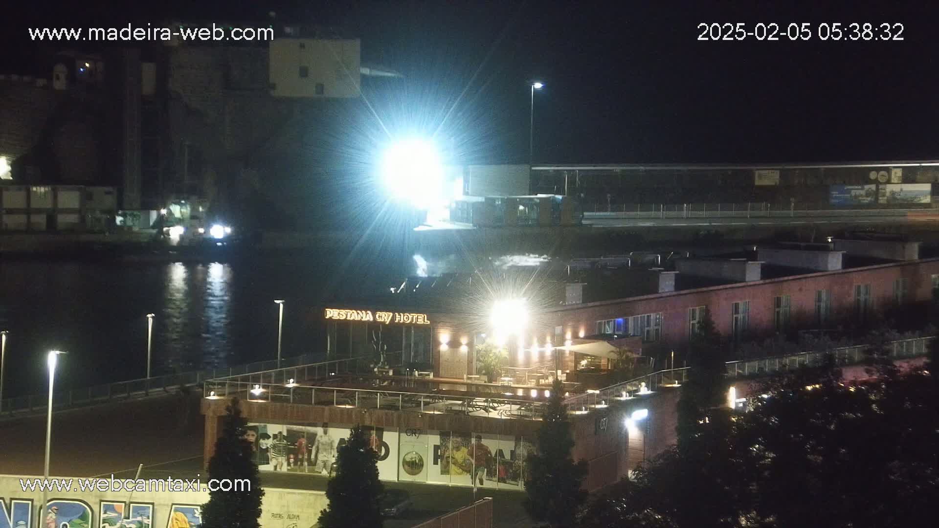 A nighttime view of a waterfront area with a hotel, illuminated buildings, and a body of water reflecting lights.