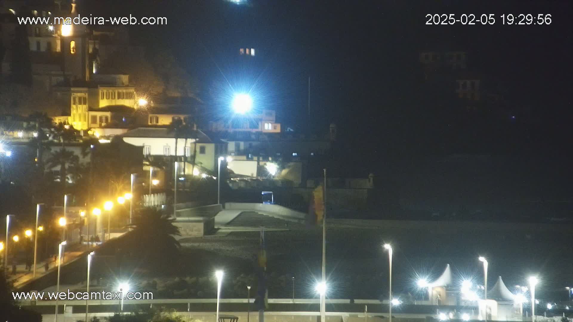 A nighttime view of a coastal town, illuminated by streetlights, with a beach area in the foreground.