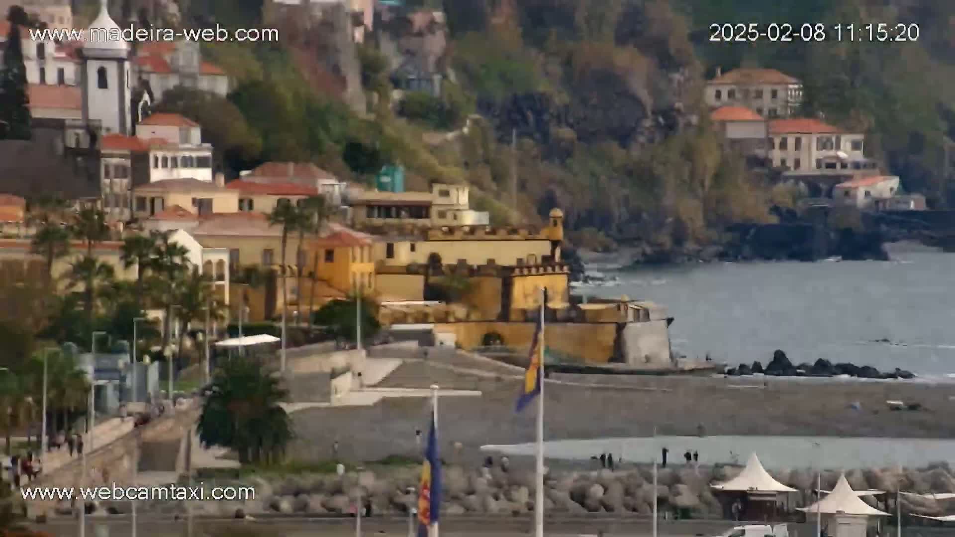 A coastal town with buildings of various colors, including a large yellow structure near the water, is shown on an overcast day.