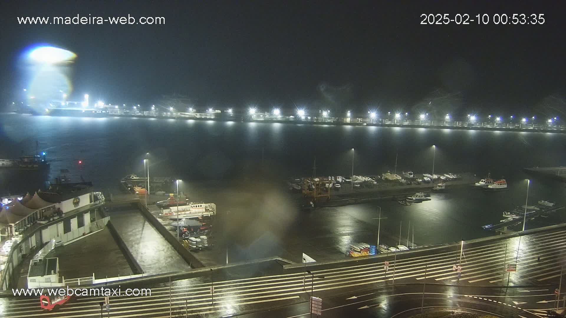 A nighttime view of a harbor with many boats docked, under rainy conditions.