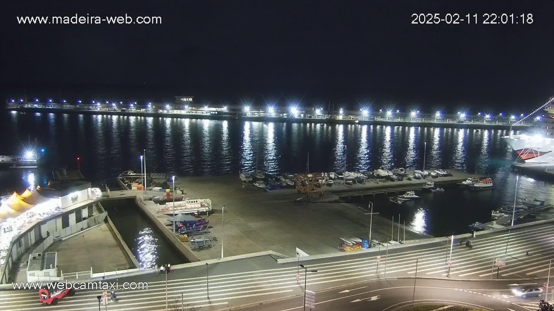 A nighttime view of a harbor filled with boats, illuminated by lights reflecting on the calm water.